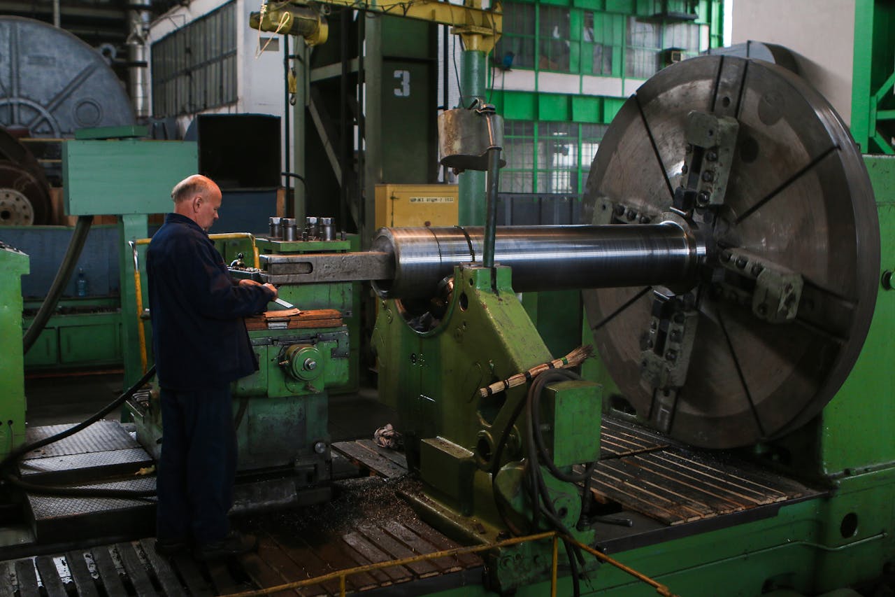 Adult male worker inspecting large machinery in an industrial factory setting.