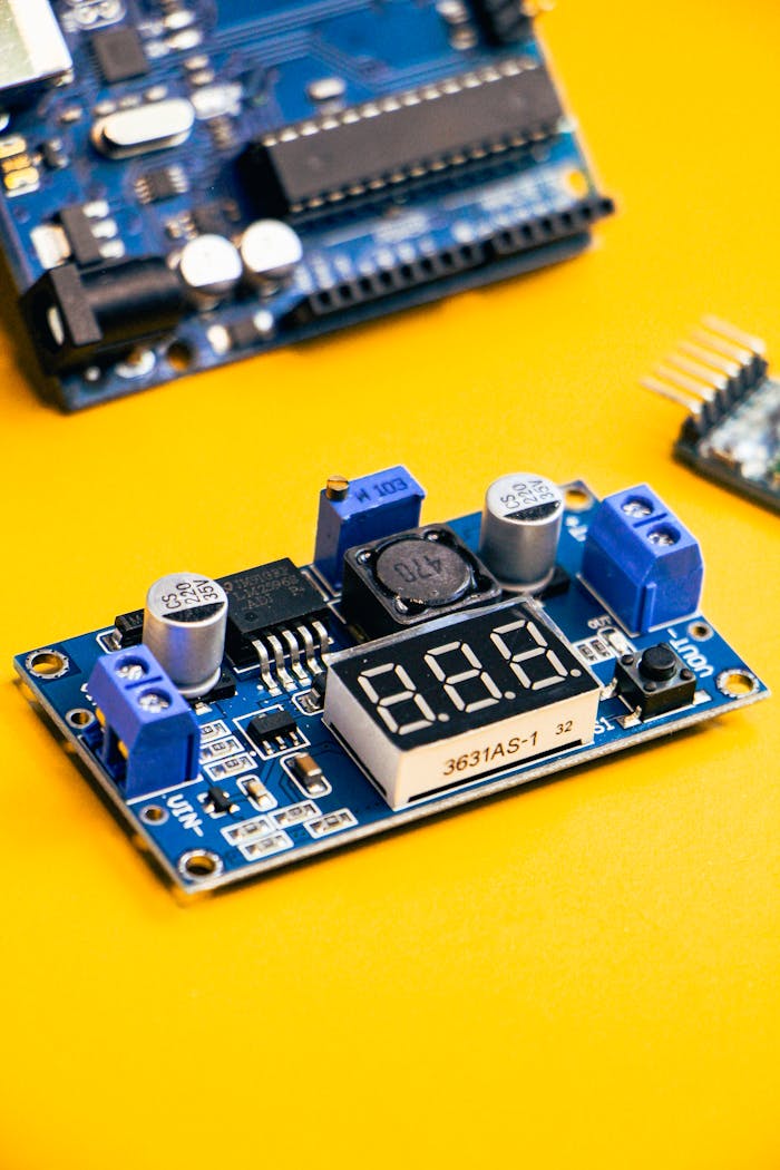 Close-up of an electronic circuit board with digital display on a vibrant yellow background.